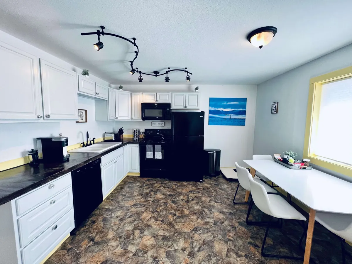 The image features a bright dining area with white cabinetry and black appliances, suggesting a kitchen-dining combination. A dining table invites group meals, while decorative wall art adds a touch of personality. The ambiance is cozy, perfect for both family dinners and casual entertaining.