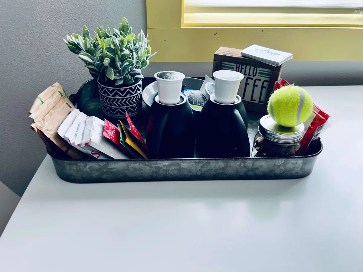 This cozy vignette showcases a coffee and snack station, complete with condiments, a potted plant, and a decorative sign. The arrangement suggests a welcoming spot for casual bites, morning coffee, or planning the day ahead, all within a warm, inviting atmosphere.